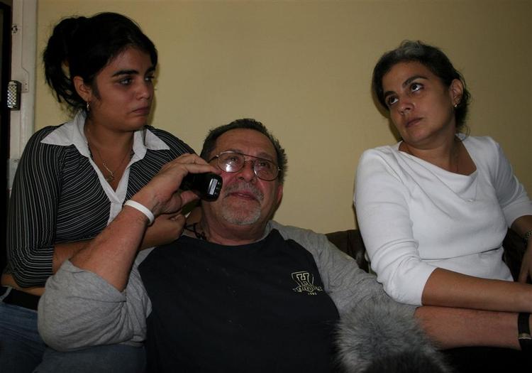 Hector Palacios (i midten) taler i telefon, mens hans datter, Gisel Recaren (t.v.) og hans kone Gisela Delgado sidder omkring ham i huset i Havana. 
