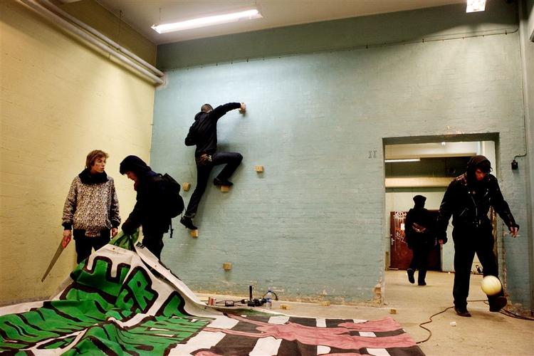 Der er livlig aktivitet i det besatte hus på Dortheavej. Mens en klatrer på en hurtigt lavet klatrevæg, er et par stykker i gang med at lave en banner. 