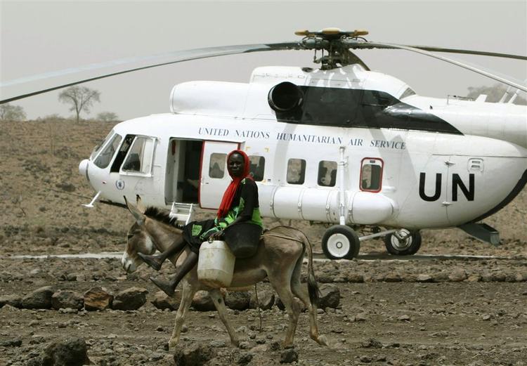 En kvinde, ridende på et æsel, passerer en helikopter med vandforsyninger. 