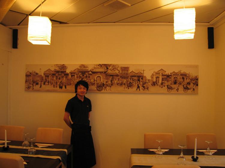 Sønnen Hao Li i restauranten foran et stofmaleri, som familien har købt med hjem fra Kina. 