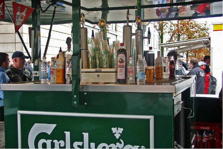 Ølstaderne rundt om Parken gemmer andet end bare øl. Adskillige varianter af vodkashots kan frit nydes, inden fodbolden bliver givet fri inden for murene (øverst). For få måneder siden kastede Parken sig ligeledes ud i salg af spiritus på mere mobil vis. Her er det danske roligans, der slukker tørsten inden landskampen mod Nordirland i efteråret (th.) Foto: Privat 