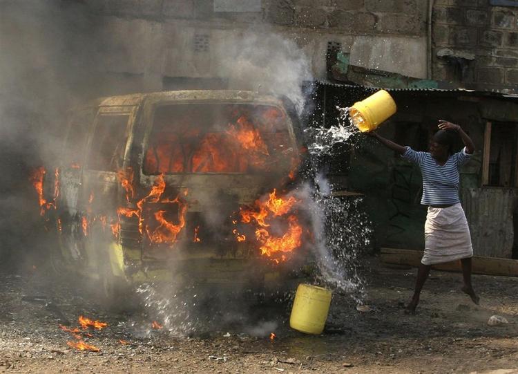 En kvinde forsøger at slukke ilden i en brændende taxa i Nairobi i kølvandet på sammenstød mellem Mungiki-medlemmer og politiet. 
