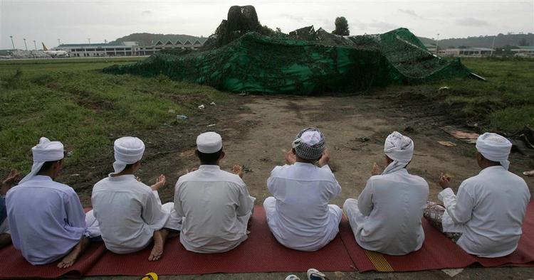 Muslimske ledere beder for de omkomne nær det tildækkede vrag af flyet, det styrtede ned på ferieøen Phuket under landing søndag i en regnstorm. 