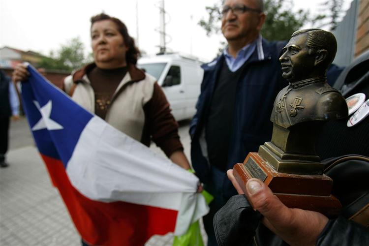 Støtter af Chiles tidligere diktator Augusto Pinochet har taget opstilling uden for politiets hovedkvarter i Santiago. Med sig har de landets flag og en buste af den afdøde diktator, der skal markere støtten til Pinochets familie og venner, der er blevet anholdt og sigtet for korruption. 