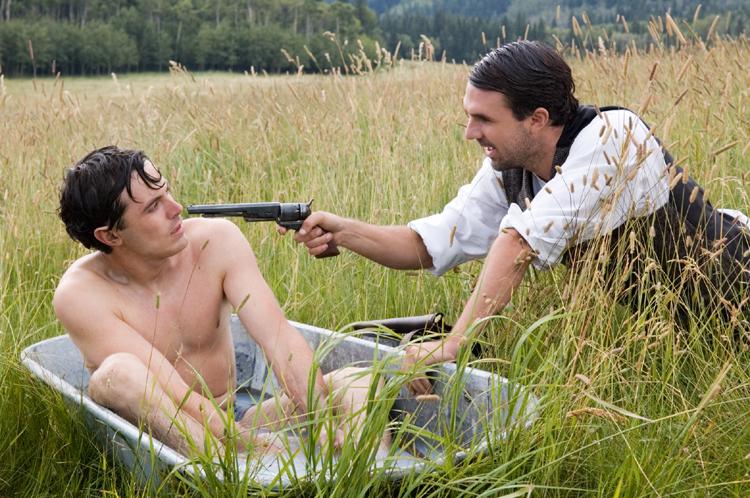 Morderspiren og grønskollingen Robert Ford (tv., Casey Affleck) befinder sig også i den forkerte ende af skyderen, her bandemedlemmet Dick Liddils (Paul Schneider). 