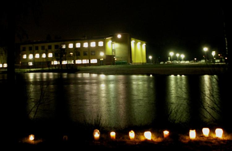 Eleverne har tændt lys ved søens bred. På den anden side af vandet ligger skolen. 
