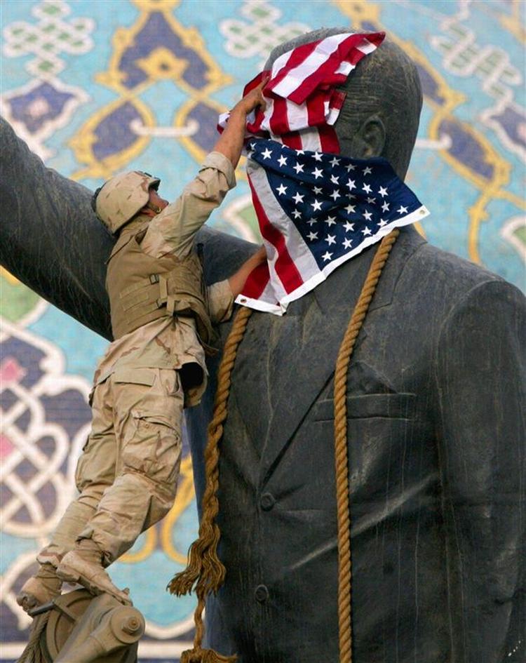 En amerikansk marinesoldat placerer det amerikanske flag på hovedet af en statue af Saddam Hussein, før statuen væltes i april 2003 efter den amerikansk-anførte invasion. Arkivfoto. 