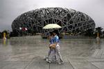 To kinesere spadserer foran det stadium i Beijing, som skal danne ramme om åbningsceremonien ved OL. Det bliver kaldet 'fuglereden' på grund af sit karakteristiske udseende. 