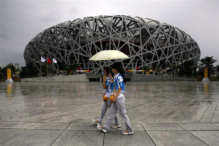 To kinesere spadserer foran det stadium i Beijing, som skal danne ramme om åbningsceremonien ved OL. Det bliver kaldet 'fuglereden' på grund af sit karakteristiske udseende. 