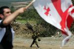 En georgier vifter et georgisk flag ved en demonstration i byen Igoeti i går. I baggrunden går en russisk soldat. De seneste dage har russiske soldater bygget vagtposter og gravet skyttegrave forskellige steder i Georgien, hvor de planlægger at blive. 
