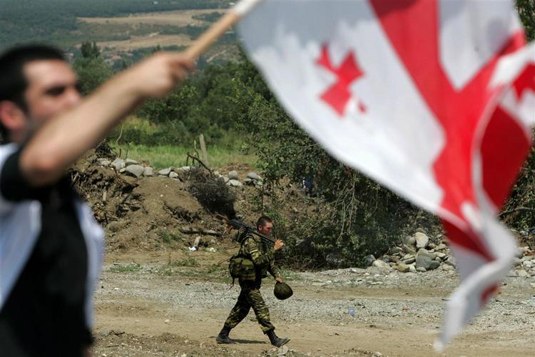 En georgier vifter et georgisk flag ved en demonstration i byen Igoeti i går. I baggrunden går en russisk soldat. De seneste dage har russiske soldater bygget vagtposter og gravet skyttegrave forskellige steder i Georgien, hvor de planlægger at blive. 