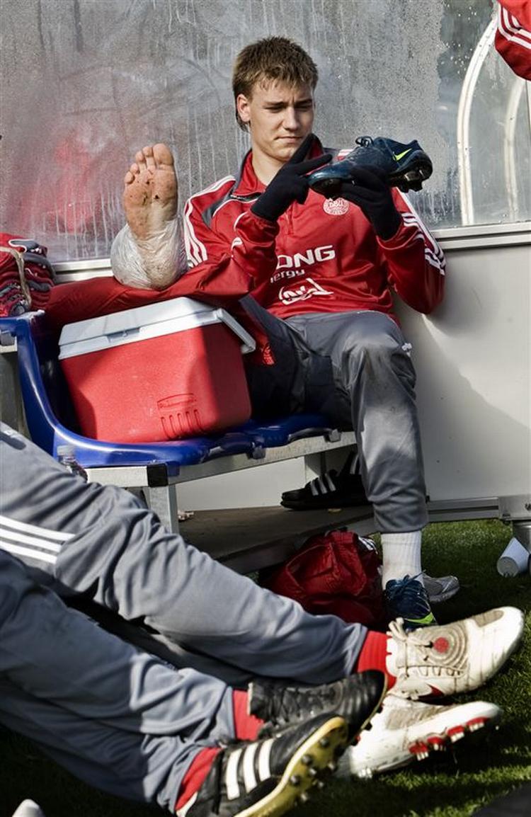 En skadet Nicklas Bendtner holder benet oppe og inspicerer sin støvle. 