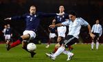 Carlos Tevez sparker, mens Skotlands Alan Hutton ser på. 