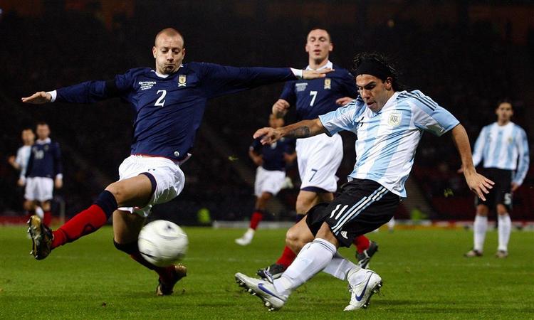 Carlos Tevez sparker, mens Skotlands Alan Hutton ser på. 