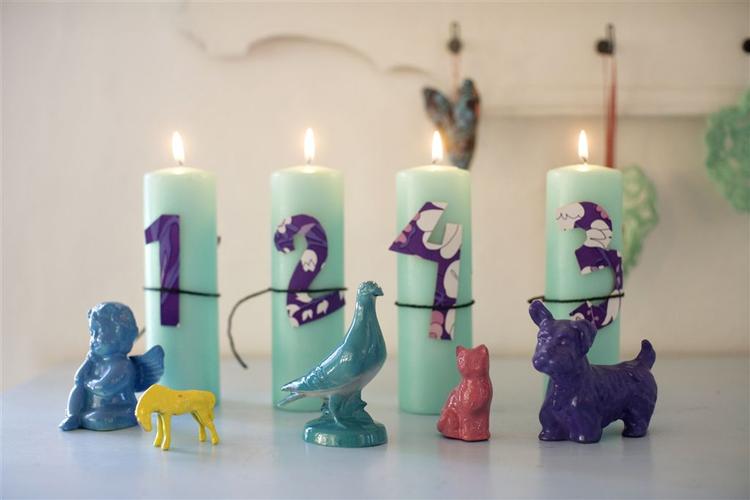 BARNLIG ADVENTSKRANS. Fire mintgrønne bloklys stillet på række med tal af tapeter bundet omkring lysene med en sort snor. Porcelænsdyr fundet i en genbrugsbutik er spraymalet i forskellige farver. 