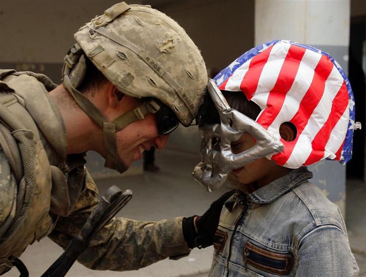 En amerikansk soldat på besøg på en irakisk skole i Mosul. Drengen er iklædt en football-hjelm svøbt i det amerikanske flag. 