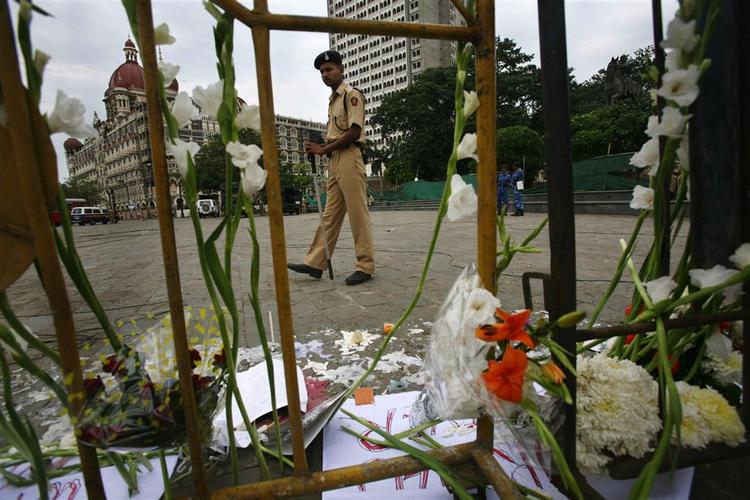En indisk politimand går forbi en række blomster og stearinlys ved et mindested for ofrene i terrorangrebet. I baggrunden ses Taj Mahal-hotellet. 