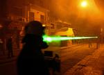 Skjulte græske demonstranter bruger laserlys mod en politiofficer under et af gadeslagene mellem unge oprørere og politiet i Athen. 
