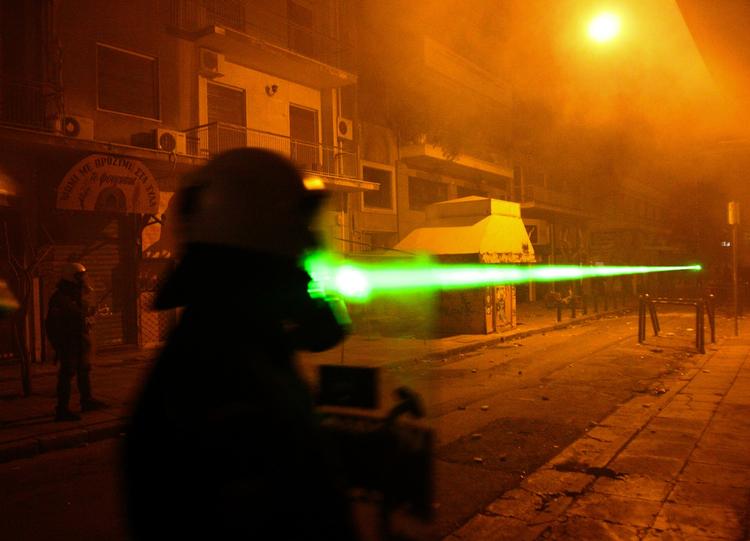 Skjulte græske demonstranter bruger laserlys mod en politiofficer under et af gadeslagene mellem unge oprørere og politiet i Athen. 