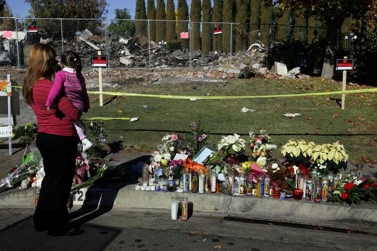 En mor og hendes barn foran det nedbrændte hus i Californien, hvor der er lagt blomster efter ni mennesker blev dræbt. 