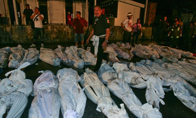 Ofrene ligger indhyllet i ligposer på gaden foran natklubben i Bangkok, hvor politifolk efterforsker dødsbranden. 