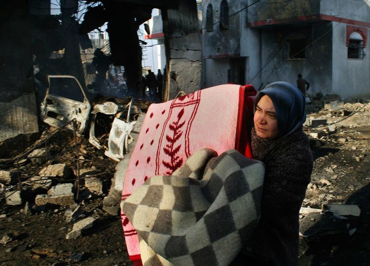 En kvinde bærer familiens ejendele   ud af ruinerene efter et bombardement mod Hamas huse i et tætbefolket område i Rafah. 