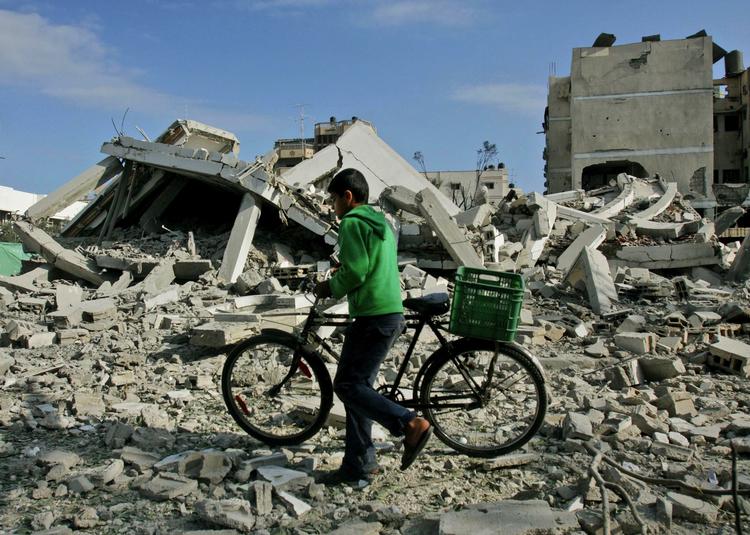 En ung palæstinenser trækker sin cykel igennem murbrokkerne efter et israelsk angreb. 