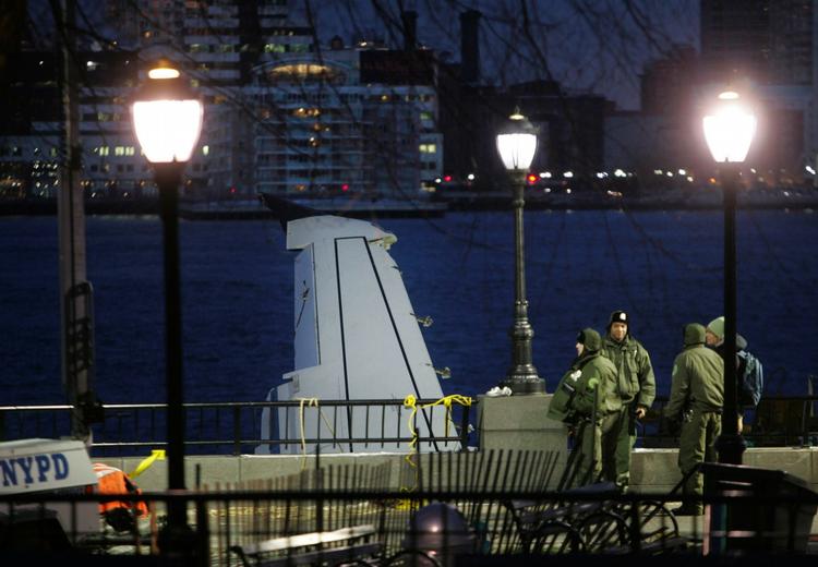 Sikkerhedspersonale bevogter det nødlandede fly, som er spændt fast til en havnekaj på Hudson Floden. 