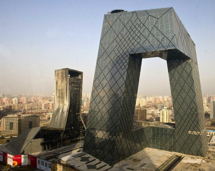 Solen står op over Beijing efter en nat, der har forvandlet hotel Mandarin Oriental (til venstre) til et tomt skelet. Bygningen til højre er tv-stationen CCTV's hovedkvarter. 
