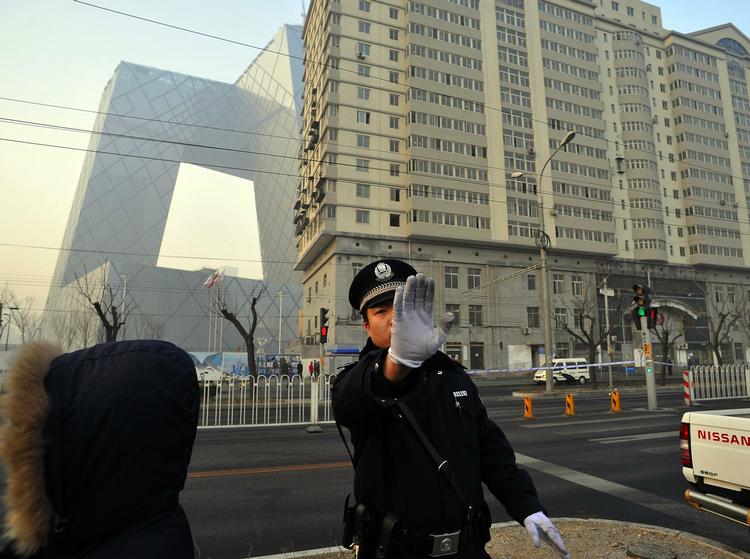 En kinesisk politimand forsøger at holde medierne væk fra området, hvor det brændte hotel og CCTV's hovedsæde ligger. 