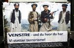 Plakat som gengiver foto af finansminister Lars Løkke Rasmussen (V), som holder en AK47-riffel i hånden, efter han har leveret 600.000 kr. til afghanske mujahediner. Til venstre for Løkkes står Asmat Mojaddedi, som er formand for Muslimernes Fællesråd. 