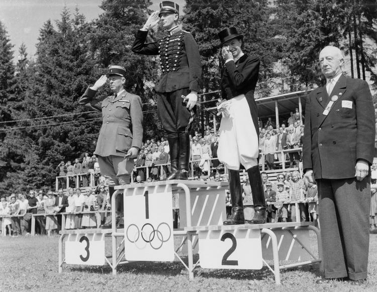 Et historisk øjeblik i OL's historie: Guldvinderen Henri Saint-Cyr fra Sverige er blankeret af franskmanden André Jousseaume og Lis Hartel efter dressurkonkurrencen. Det var første gang, der var både en mand og en kvinde på en olympisk sejrsskammel. Arkivfoto. 