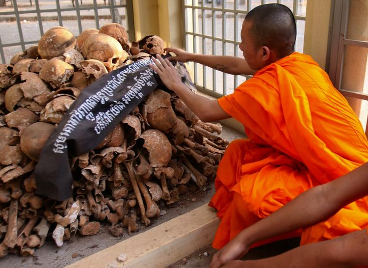 En cambodjansk munk ved utallige menneskekranier. Hele det cambodjanske folk forventes at følge med i retssagen, som bliver vist i en direkte tv-transmission. 