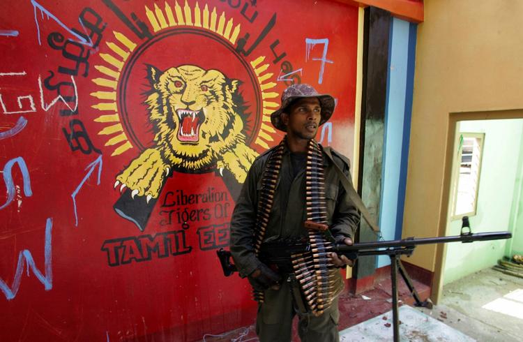 Regeringssoldat står vagt foran en forladt bygning, med De Tamilske Tigres (LTTE) karakteristiske røde flag i baggrunden prydet af en gul tiger. LTTE har lidt et historisk stort tab i kampe mod regeringshæren, som midlertidigt er standset. 
