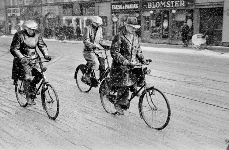 Tre mænd cykler gennem byen i snevejr. Flere af vintrene i besættelsesårene var meget hårde. 
