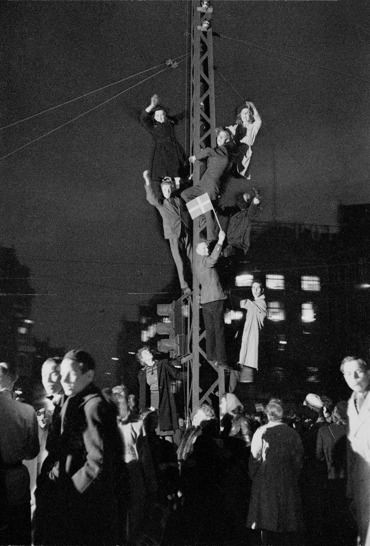 På befrielsesaftenen mødtes glade københavnere på gaden, mens andre er kravlet op i en lygtepæl med et flag. 