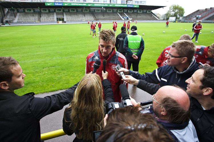 Bendtner omringet af danske og svenske mikrofonholdere på det spartanske Söderstadion i Stockholm. 