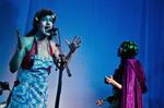 Til venstre svanser vidunderbarnet  Rosie rundt og  synger opera,  spiller harpe og  piano, og ved siden af hende optræder den indesluttede Coco i mørklilla kappe og med et stramt tørklæde om hovedet.  Foto: Sara Galbiati 