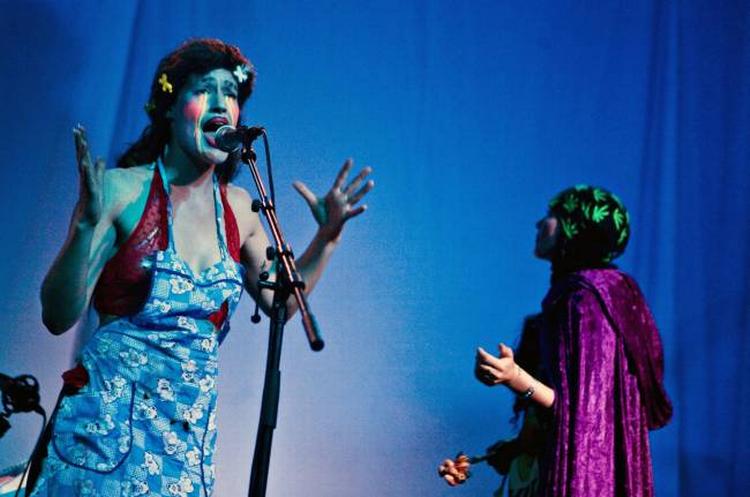 Til venstre svanser vidunderbarnet  Rosie rundt og  synger opera,  spiller harpe og  piano, og ved siden af hende optræder den indesluttede Coco i mørklilla kappe og med et stramt tørklæde om hovedet.  Foto: Sara Galbiati 
