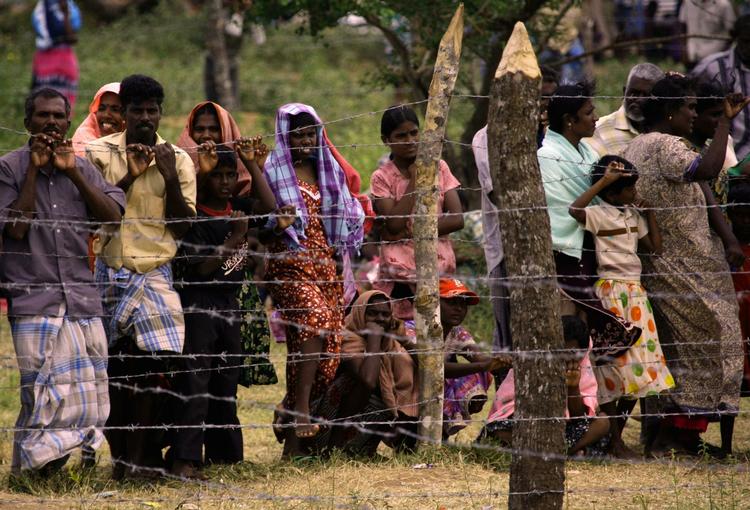 Civile står bag et pigtrådshegn ved en flygtningelejr i det nordlige Sri Lanka. 