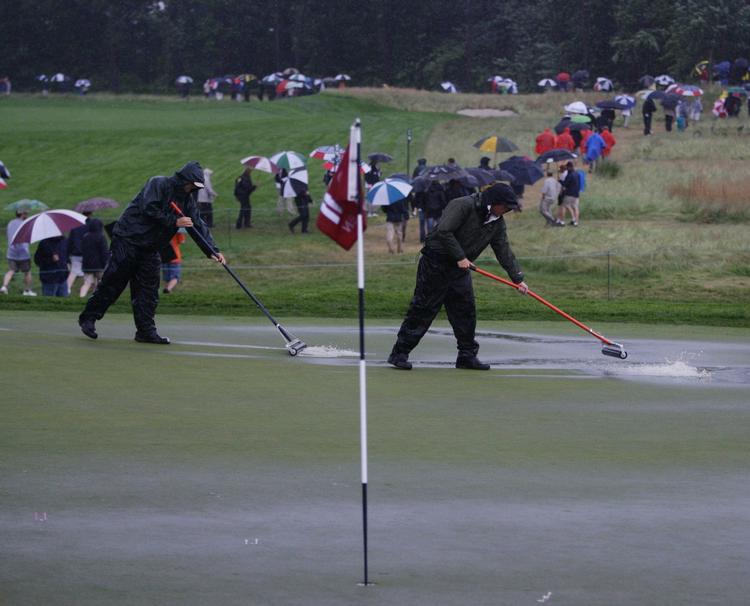 Frivillige er i gang med at fjerne vandmasserne, der har oversvømmet greens på US Open-banen. 