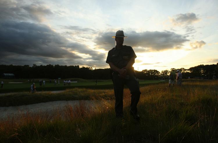 En politimand holder øje med sikkerheden for golf-stjernerne ved US Open, mens skyerne trækker sammen til regn. 