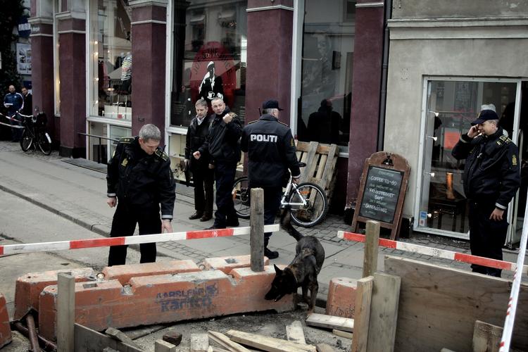 Politi med hunde  leder efter spor foran juicebaren, hvor HA-rockeren Brian Sandberg blev forsøgt likvideret. I dag blev den ene af attentatmændene sigtet - han sad allerede i fængsel for en anden forbrydelse. Arkivfoto. 