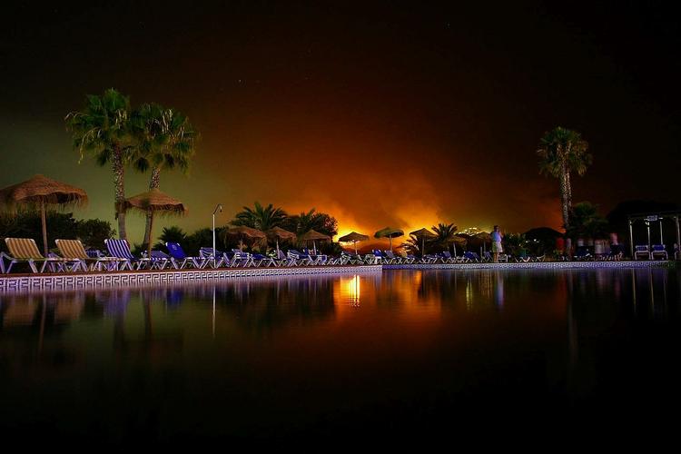 En mand ved en svømmepøl betragter en skovbrand i spanske Turre.  I den nærliggende ferieby Mojacar er 1.500 mennesker blevet evakueret på grund af brandene. 
