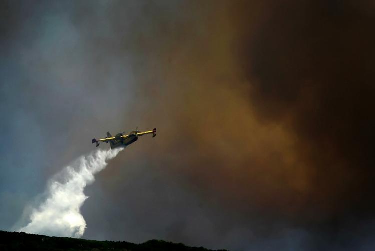 Et græsk brandslukningsfly smidder sin last af vand over flammerne. 
