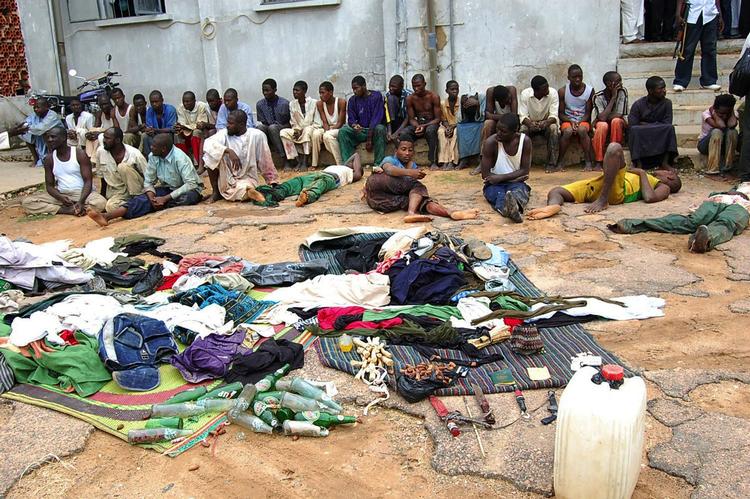 Urolighederne i Nigeria begyndte søndag. Billedet er fra mandag, hvor arresterede medlemmer af den militante islamistiske gruppe sidder uden for en politistation med deres ejendele. 
