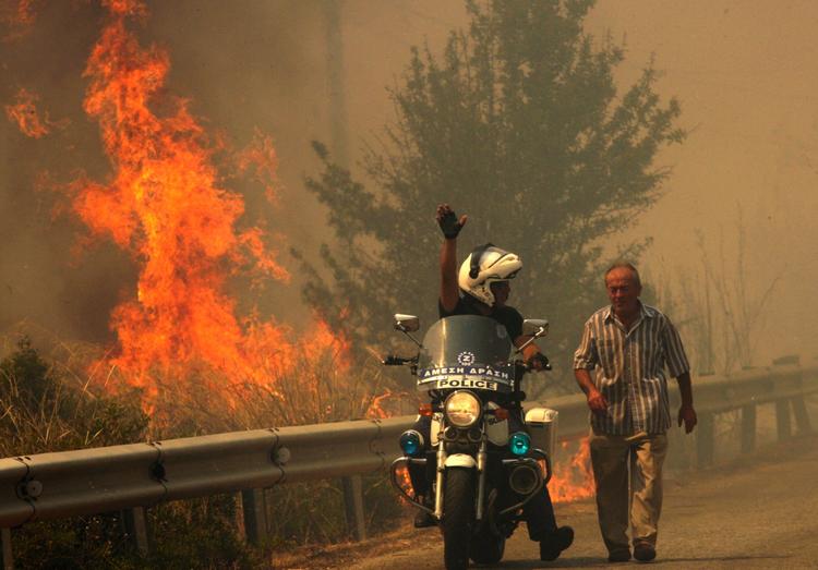 En politibetjent viser en lokalmand væk fra de voldsomme brande uden for Athen. 