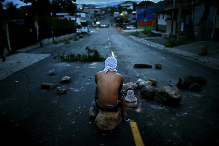 En enlig demonstrant sidder ved en vejblokade i Honduras' hovedstad. 