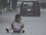 En dreng bærer sin lillebror gennem de vandmasser, der er væltet ned over deres hjem i Manila-forstaden Quezon. 