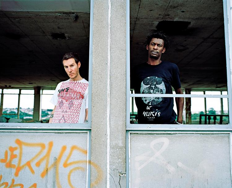 Selv om Daddy G og 3D, der i dag udgør Massive Attack ligner sig selv nogenlunde fra gruppens tidlige plakater og stadig bor i Bristol, hvor alt startede, er der sket store forandringer, mener de to i vinduet til deres studie. »Hele verden er blevet protektionistisk, og alt handler om penge. Det har ødelagt meget her«, mener de to. PR-foto: Hamish Brown 